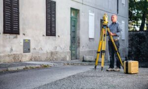 Urban property surveyor street level - ALTA SURVEY Illinois Licensed land surveyor performing an elevation survey near a residential street to measure property height