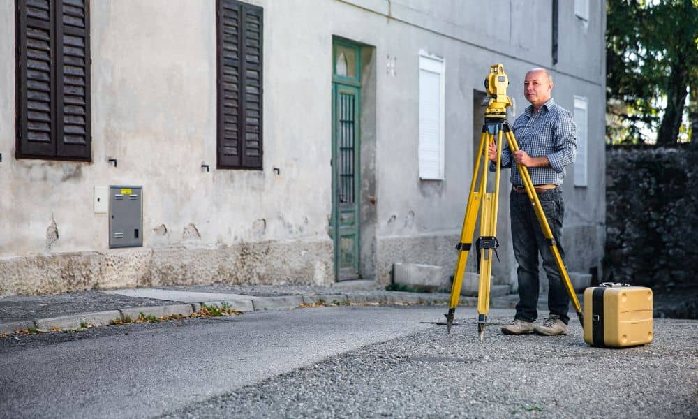 Licensed land surveyor performing an elevation survey near a residential street to measure property height
