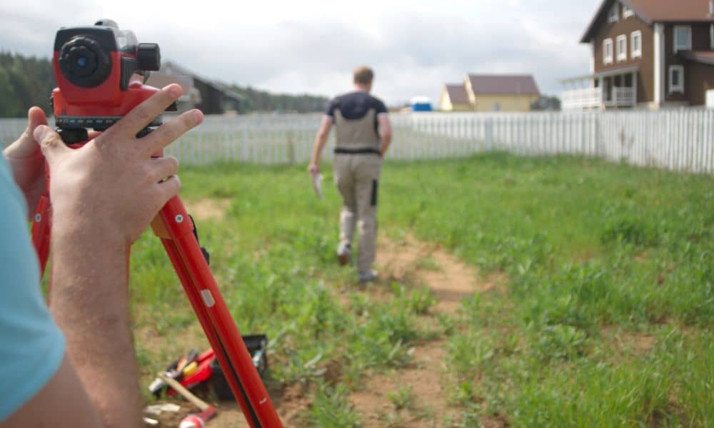 Land surveyor measuring a residential property line to complete a property line survey before building near a fence