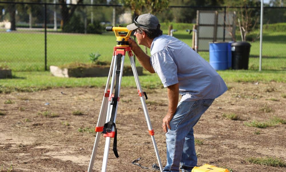 Surveyor using tripod equipment to complete a property survey on residential land before building an ADU coach house