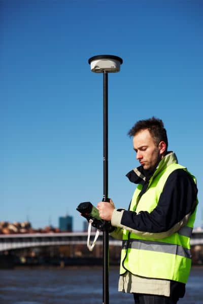 Professional surveyor using modern GPS equipment near a river to map land and water boundaries for accurate land surveying
