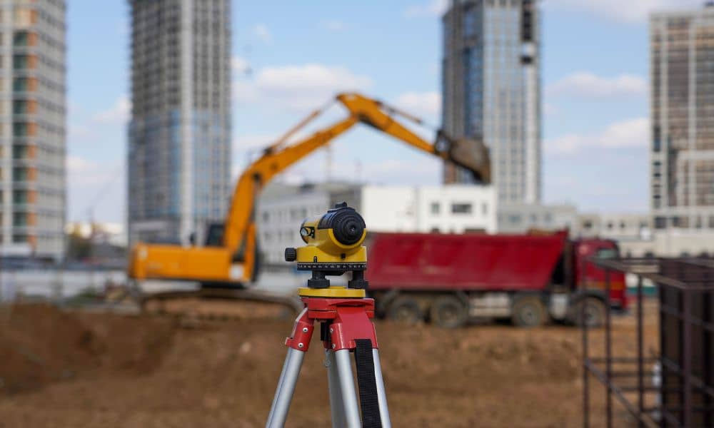 Land surveying level instrument set up at a large construction site with cranes and buildings in the background, representing an ALTA Title Survey for major projects
