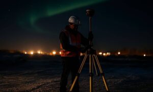 Construction surveyor using GNSS rover at night under green aurora lights