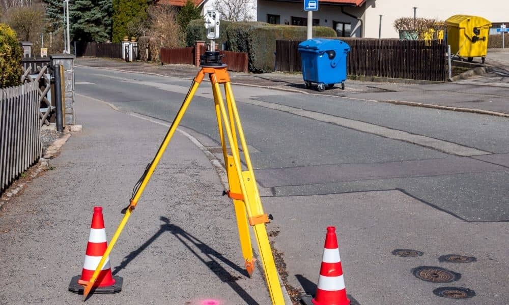 Tripod and safety cones set up for a property survey along a public sidewalk to ensure right-of-way safety and permit compliance
