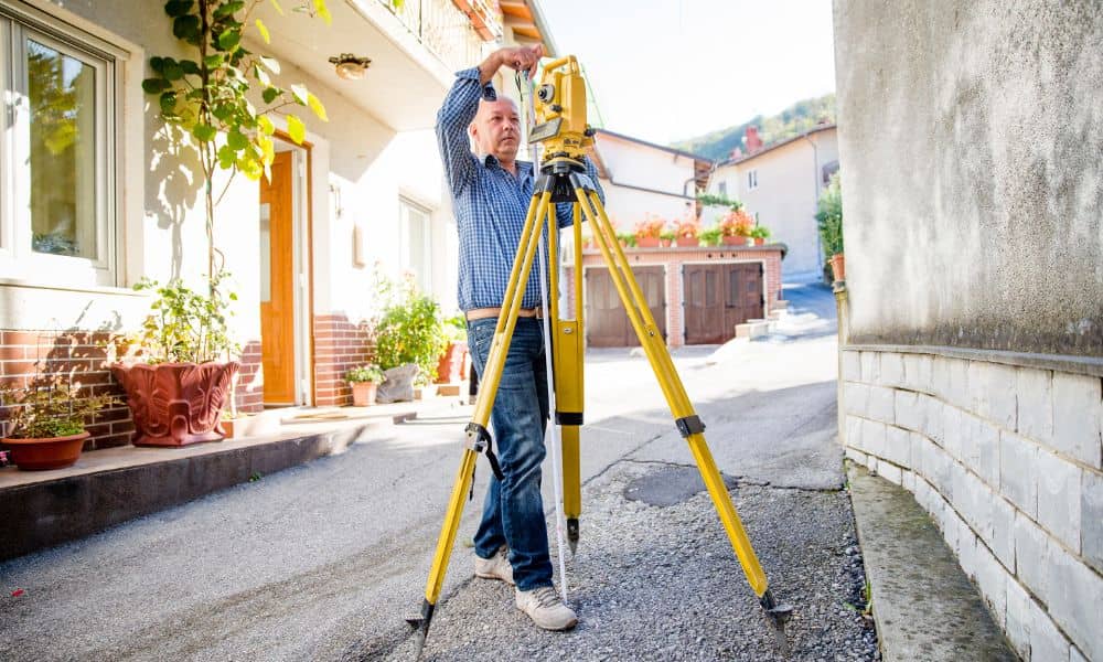 A licensed land surveyor conducting an elevation survey outside a home to help document storm and flood damage