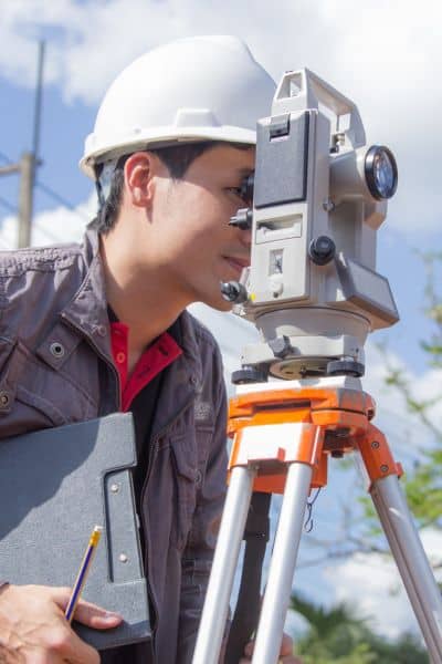 Surveyor using a total station during an ALTA land survey to verify property boundary measurements